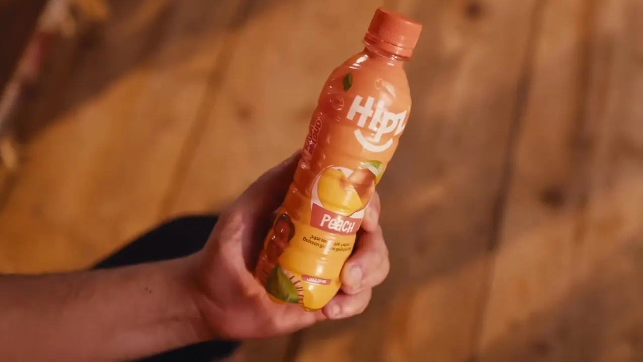 Une main tend une bouteille HIPZ Peach
